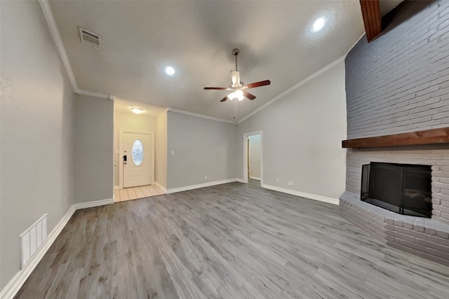 unfurnished living room featuring lofted ceiling, ornamental molding, a brick fireplace, and light hardwood / wood-style flooring