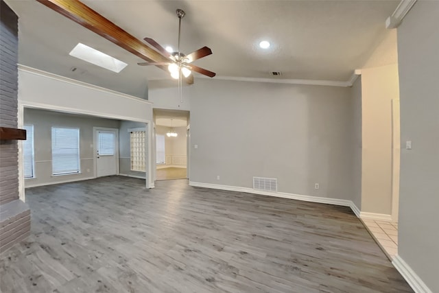 unfurnished living room with hardwood / wood-style flooring, ornamental molding, vaulted ceiling with skylight, and ceiling fan