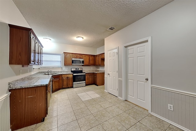 kitchen featuring light tile patterned flooring, appliances with stainless steel finishes, sink, light stone countertops, and a textured ceiling