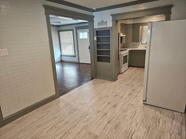 kitchen with gray cabinetry, white appliances, brick wall, and light wood-type flooring