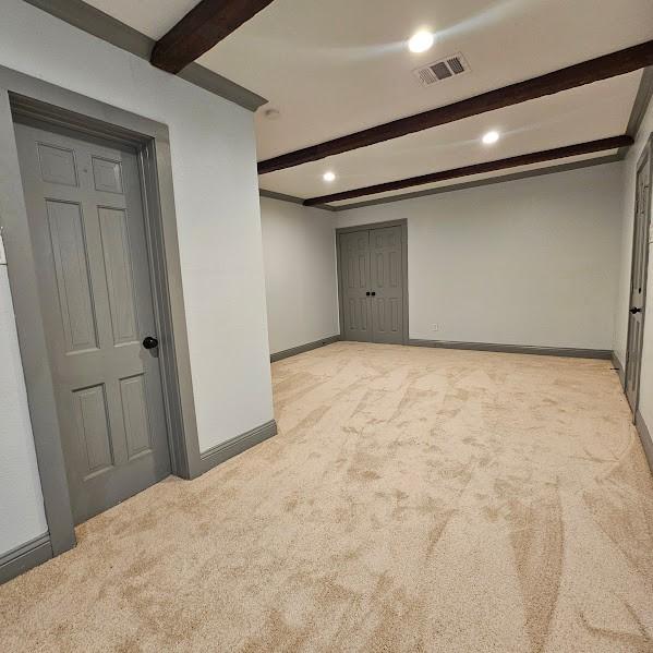 empty room featuring light colored carpet and beam ceiling