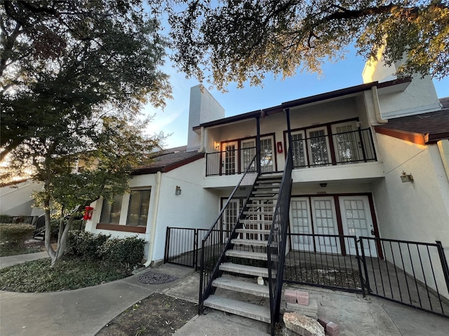 view of front of property featuring stucco siding, a chimney, stairs, and fence