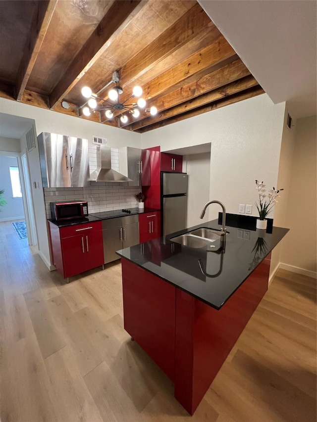 kitchen featuring dark countertops, wall chimney range hood, beamed ceiling, black appliances, and a sink