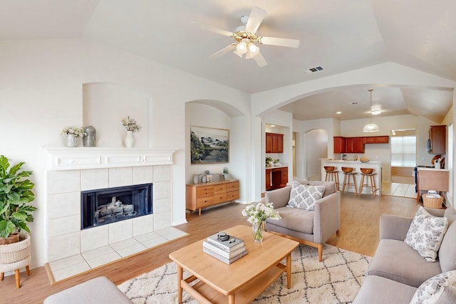 living room with a tiled fireplace, vaulted ceiling, ceiling fan, and light wood-type flooring