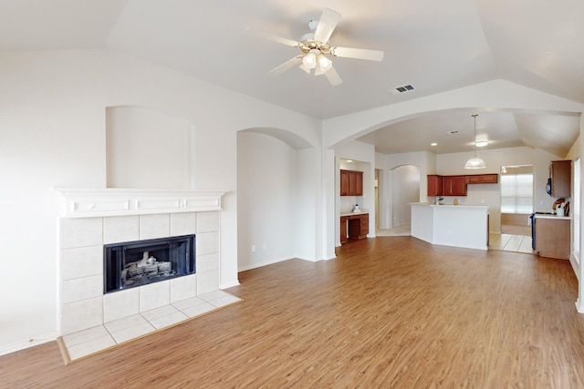 unfurnished living room with a tiled fireplace, ceiling fan, lofted ceiling, and light wood-type flooring