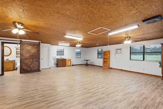 unfurnished room featuring ceiling fan, a barn door, a wall mounted air conditioner, and light wood-type flooring