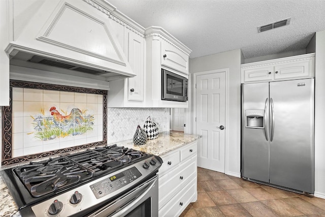 kitchen with custom exhaust hood, appliances with stainless steel finishes, light stone countertops, decorative backsplash, and white cabinets