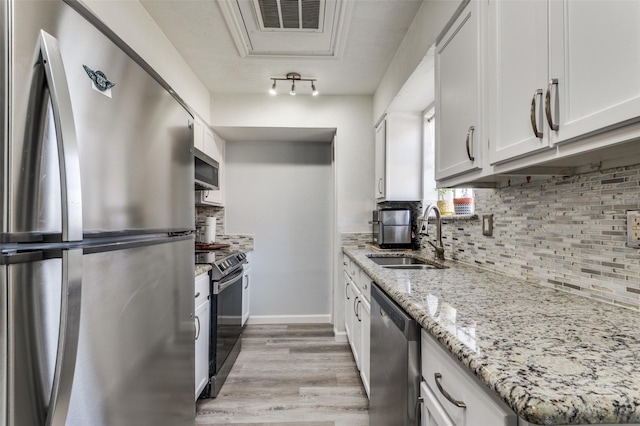 kitchen with sink, appliances with stainless steel finishes, light stone countertops, decorative backsplash, and white cabinets