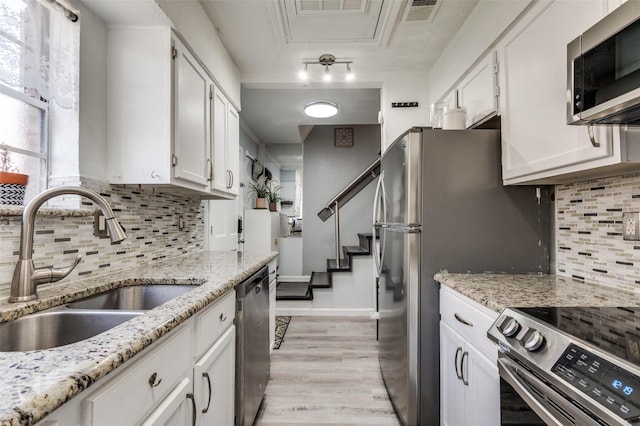 kitchen featuring appliances with stainless steel finishes, white cabinetry, sink, light stone counters, and light hardwood / wood-style floors