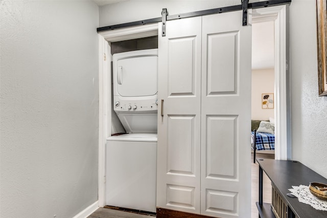 laundry area featuring a barn door, stacked washer / drying machine, and hardwood / wood-style floors