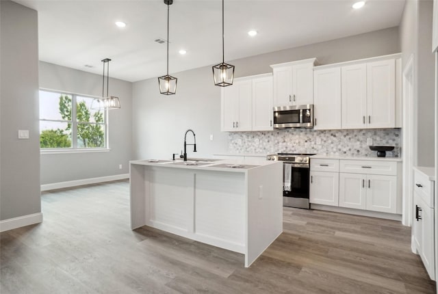 kitchen with white cabinetry, appliances with stainless steel finishes, sink, and a center island with sink