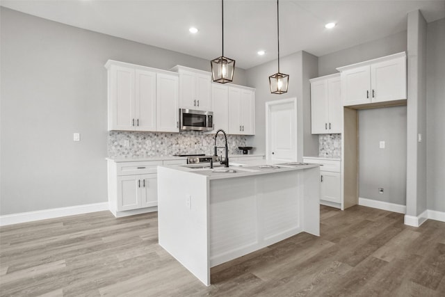 kitchen with pendant lighting, white cabinetry, tasteful backsplash, an island with sink, and light wood-type flooring