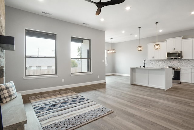 kitchen featuring pendant lighting, sink, stainless steel appliances, white cabinets, and a center island with sink