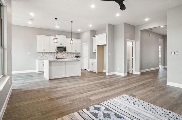 kitchen with tasteful backsplash, decorative light fixtures, light wood-type flooring, an island with sink, and white cabinets