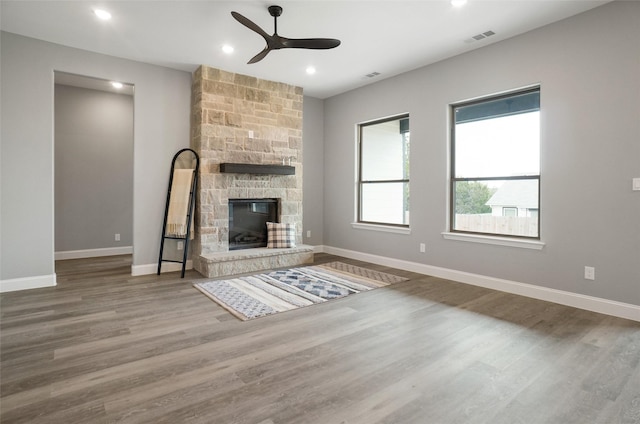 unfurnished living room featuring ceiling fan, wood-type flooring, and a stone fireplace