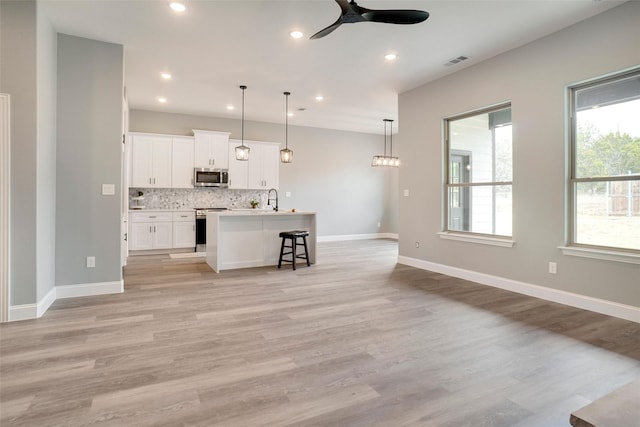 kitchen with pendant lighting, white cabinetry, stainless steel appliances, tasteful backsplash, and a center island with sink