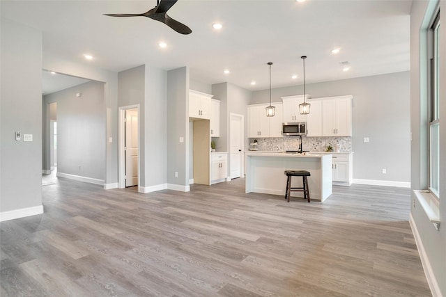 kitchen with white cabinetry, tasteful backsplash, hanging light fixtures, a center island with sink, and a kitchen breakfast bar