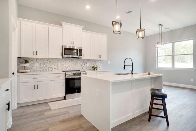 kitchen featuring sink, pendant lighting, stainless steel appliances, a kitchen island with sink, and white cabinets