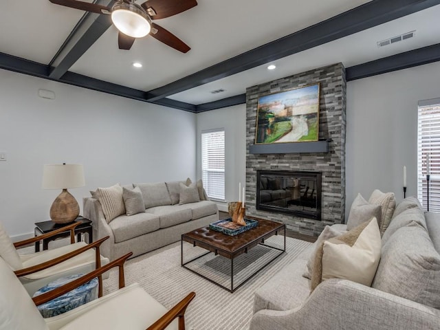 living room with ceiling fan, a healthy amount of sunlight, beam ceiling, and a stone fireplace