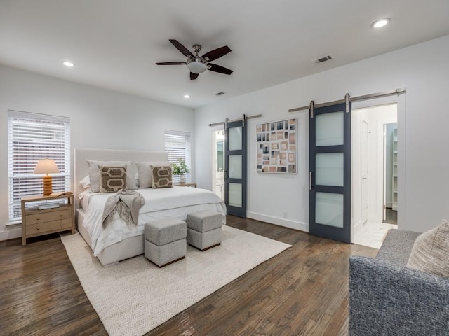 bedroom with a barn door, dark hardwood / wood-style floors, and ceiling fan