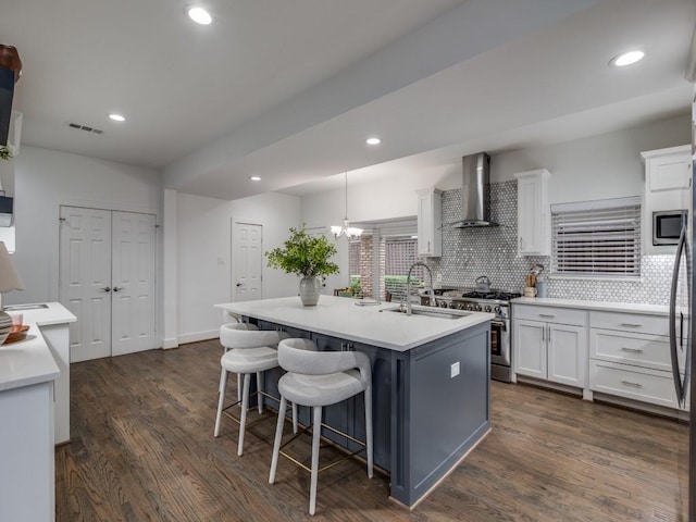 kitchen with wall chimney exhaust hood, sink, appliances with stainless steel finishes, a kitchen island with sink, and white cabinets