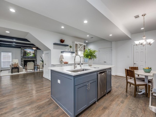 kitchen with sink, dark wood-type flooring, dishwasher, hanging light fixtures, and an island with sink