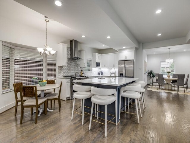 kitchen featuring pendant lighting, wall chimney range hood, white cabinets, and appliances with stainless steel finishes