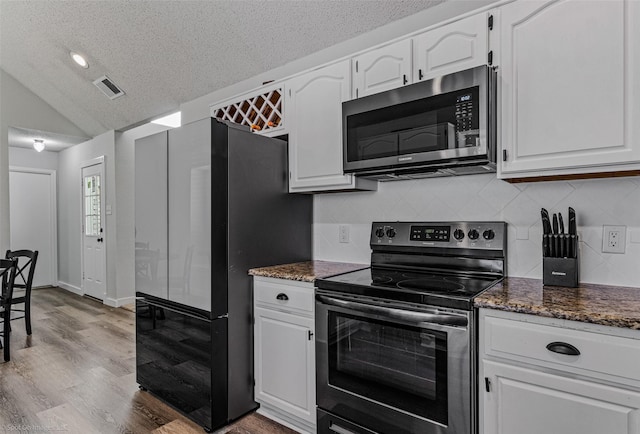 kitchen with lofted ceiling, light hardwood / wood-style flooring, dark stone counters, stainless steel appliances, and white cabinets