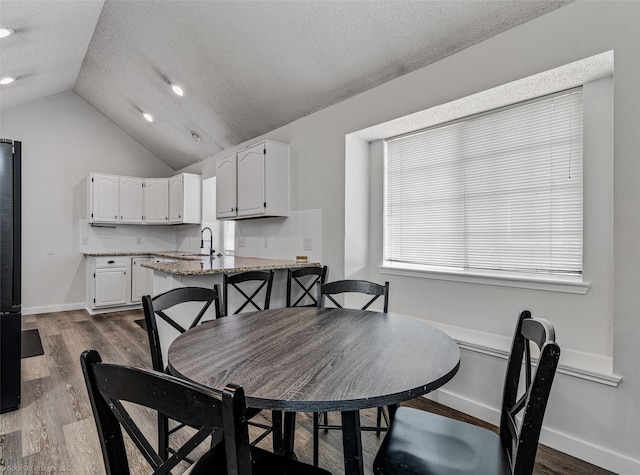 dining room featuring wood-type flooring, sink, vaulted ceiling, and a textured ceiling