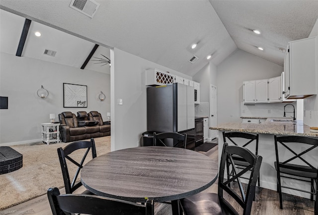 dining area with sink, ceiling fan, high vaulted ceiling, wood-type flooring, and a textured ceiling