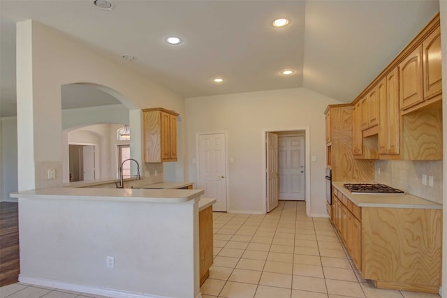 kitchen with light tile patterned flooring, lofted ceiling, light brown cabinets, appliances with stainless steel finishes, and kitchen peninsula