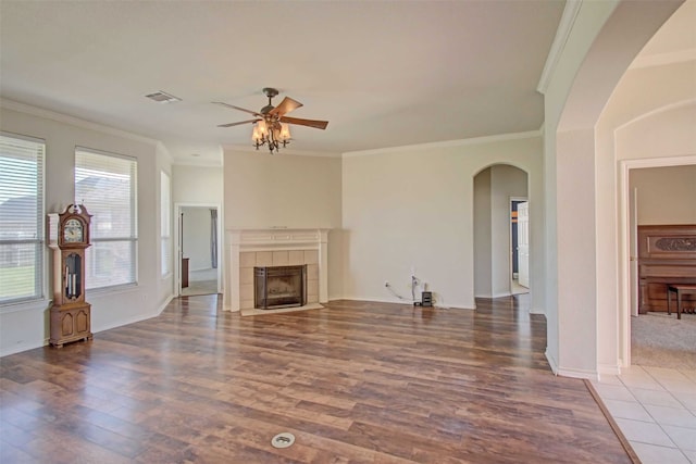 unfurnished living room with a tile fireplace, ornamental molding, wood-type flooring, and ceiling fan