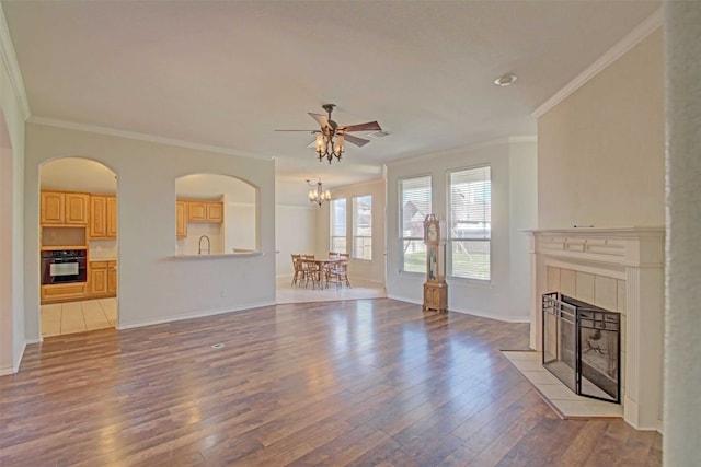 unfurnished living room featuring crown molding, ceiling fan with notable chandelier, hardwood / wood-style floors, and a tile fireplace