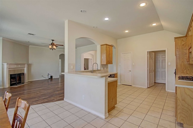 kitchen featuring lofted ceiling, light tile patterned floors, a tile fireplace, kitchen peninsula, and light brown cabinets