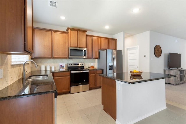 kitchen with sink, appliances with stainless steel finishes, backsplash, a kitchen island, and dark stone counters