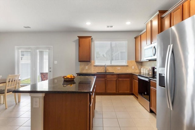 kitchen featuring sink, light tile patterned floors, appliances with stainless steel finishes, a center island, and tasteful backsplash