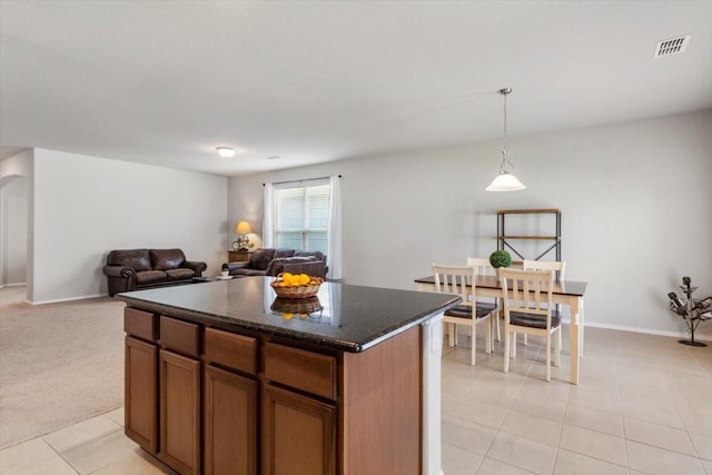 kitchen with a kitchen island, pendant lighting, light carpet, and dark stone counters