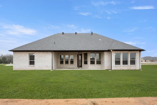 rear view of property featuring a patio area, brick siding, a lawn, and roof with shingles