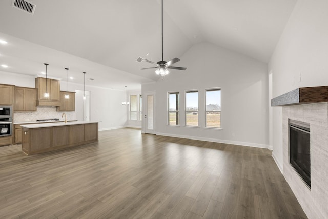 unfurnished living room with wood finished floors, a glass covered fireplace, visible vents, and a ceiling fan