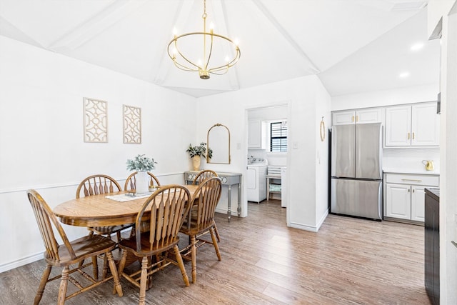 dining area featuring washer / dryer, vaulted ceiling, light hardwood / wood-style flooring, and a notable chandelier