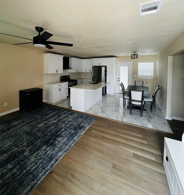 kitchen featuring sink, backsplash, black appliances, white cabinets, and a center island with sink