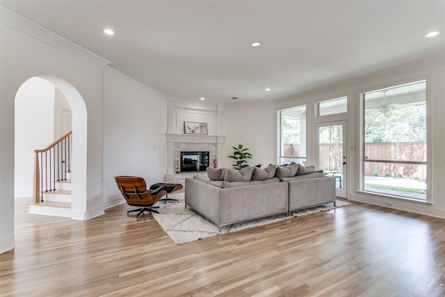 living room with a tiled fireplace, crown molding, and light hardwood / wood-style floors