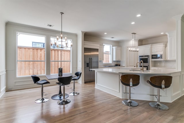 kitchen with pendant lighting, a breakfast bar, built in appliances, and white cabinets