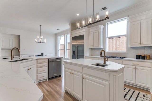 kitchen with appliances with stainless steel finishes, a kitchen island with sink, sink, and decorative light fixtures