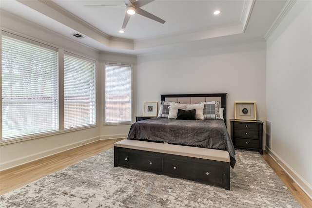 bedroom featuring crown molding, a tray ceiling, light hardwood / wood-style flooring, and ceiling fan