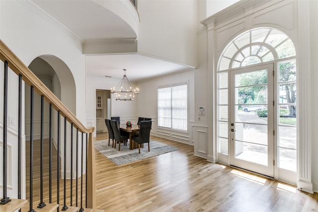 foyer with a high ceiling, crown molding, an inviting chandelier, and light wood-type flooring