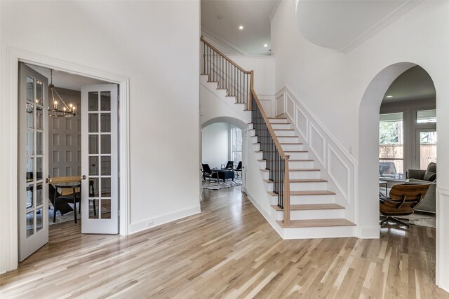 entrance foyer featuring crown molding, a towering ceiling, french doors, a chandelier, and light wood-type flooring