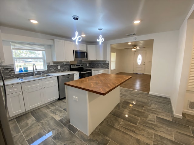 kitchen with sink, appliances with stainless steel finishes, white cabinetry, a kitchen island, and wood counters