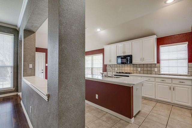 kitchen featuring sink, a center island with sink, light tile patterned floors, decorative backsplash, and white cabinets