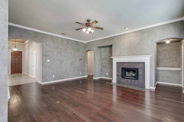 unfurnished living room with dark hardwood / wood-style flooring, a tiled fireplace, crown molding, and ceiling fan